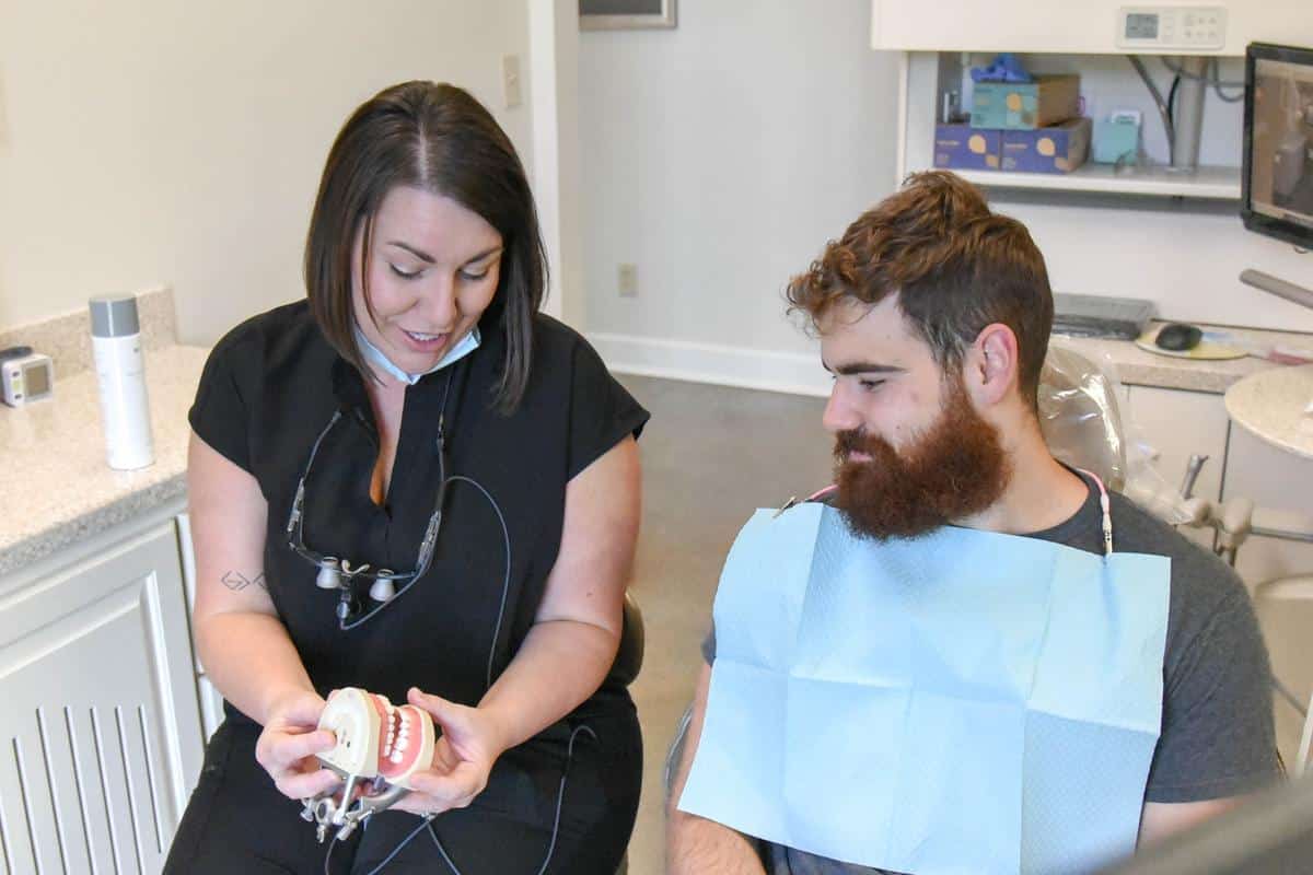 Dental team member showing tooth model to patient