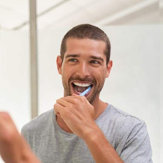 man looking in mirror and brushing teeth