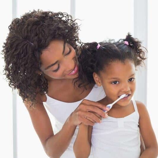 mother helping daughter brush teeth