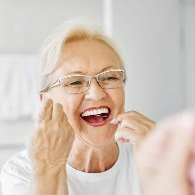 senior woman looking in bathroom mirror brushing teeth