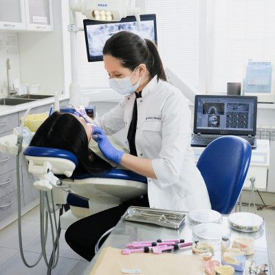 a woman in a white coat and mask working on a patient, representing what to expect during a dental exam